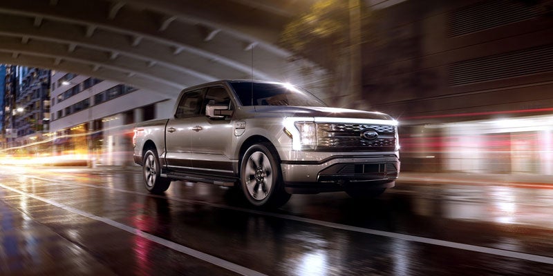 Ford F-150 Lightning plateado conduciendo bajo un puente urbano