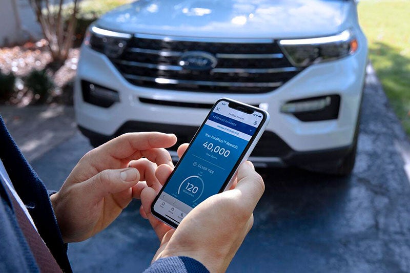 Primer plano de un teléfono móvil en la mano de un hombre que programa una cita, con un SUV Explorer® blanco al fondo