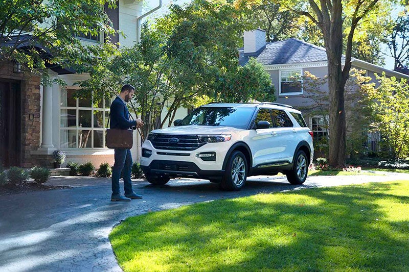 Plano exterior de un hombre frente a una casa, con un teléfono móvil y un todoterreno Explorer® blanco en la mano